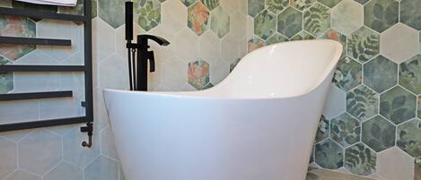 A modern bathroom with a freestanding bathtub, a towel rack, and a hexagonal tile backsplash.