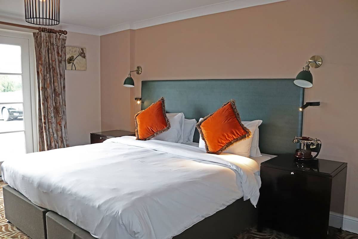 A hotel room with a large bed, two bedside tables, a nightstand, a lamp, and a window with curtains.