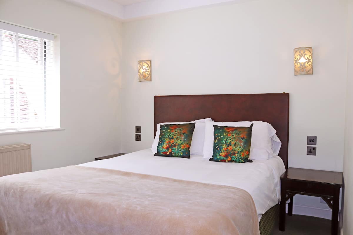 A neatly made bed with floral pillows, a wooden headboard, and two wall sconces.