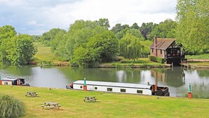 A riverside view with a house, picnic tables, and a boat docked by the water. - Shillingford Bridge Hotel (Wallingford)