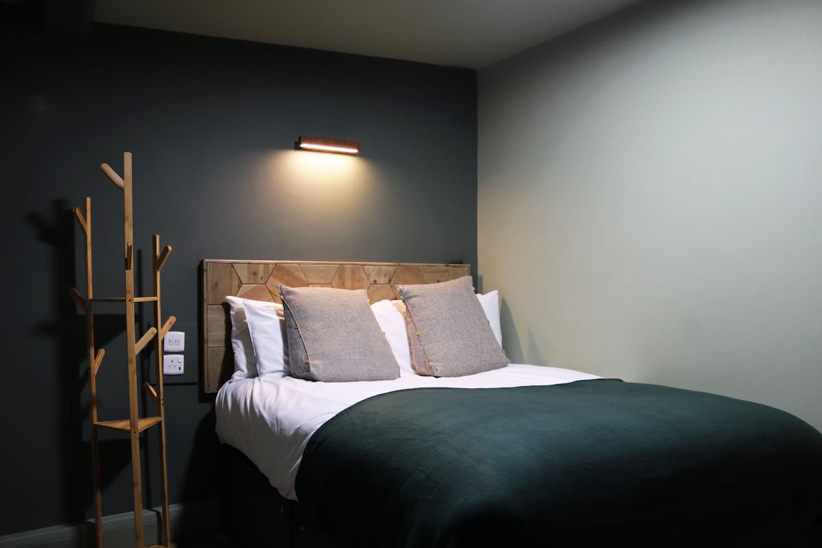 A neatly made bed with a wooden headboard, a bedside ladder, and a wall-mounted light fixture.