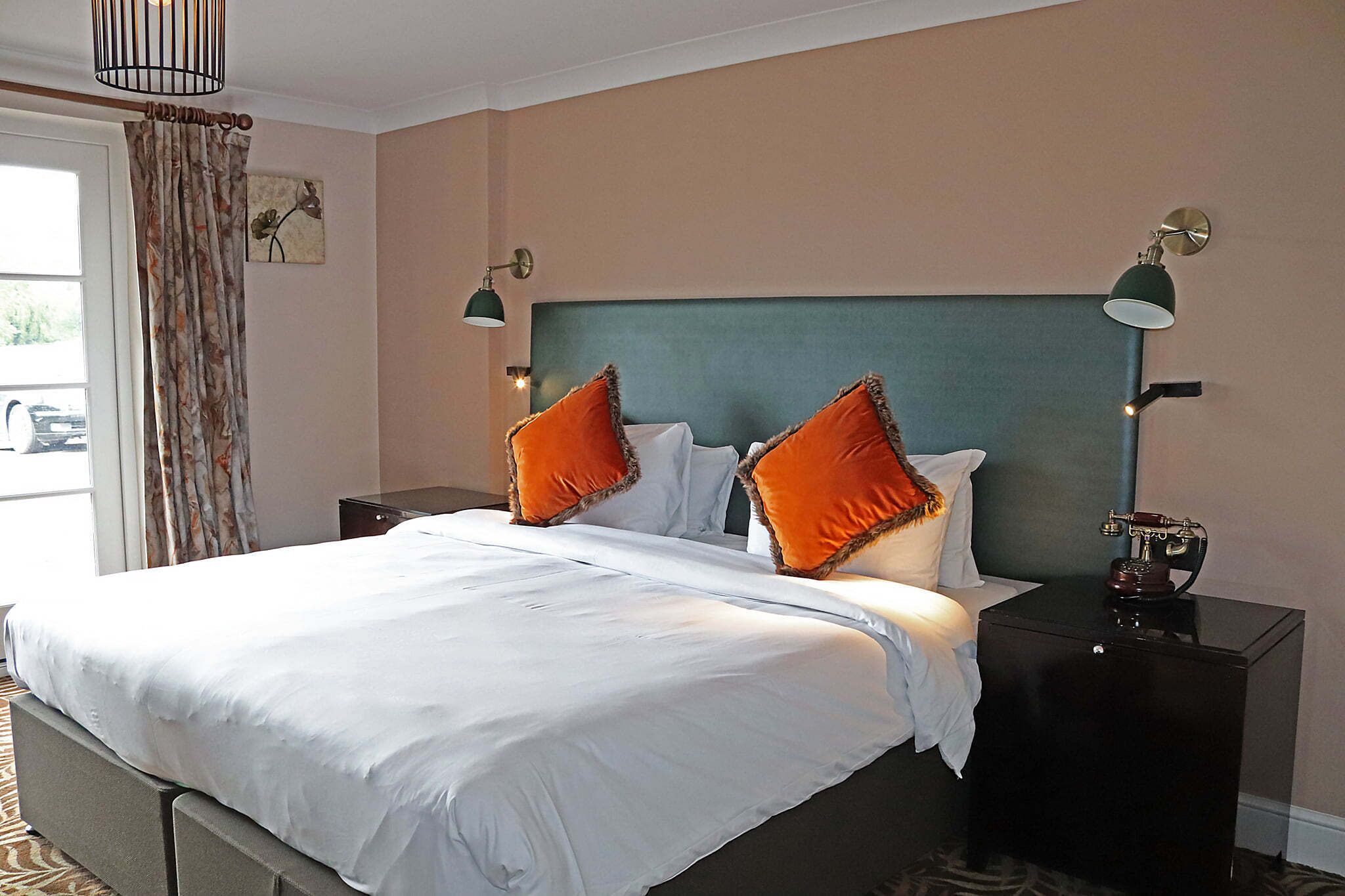 A hotel room with a bed, two nightstands, a lamp, and a view of the outside.
