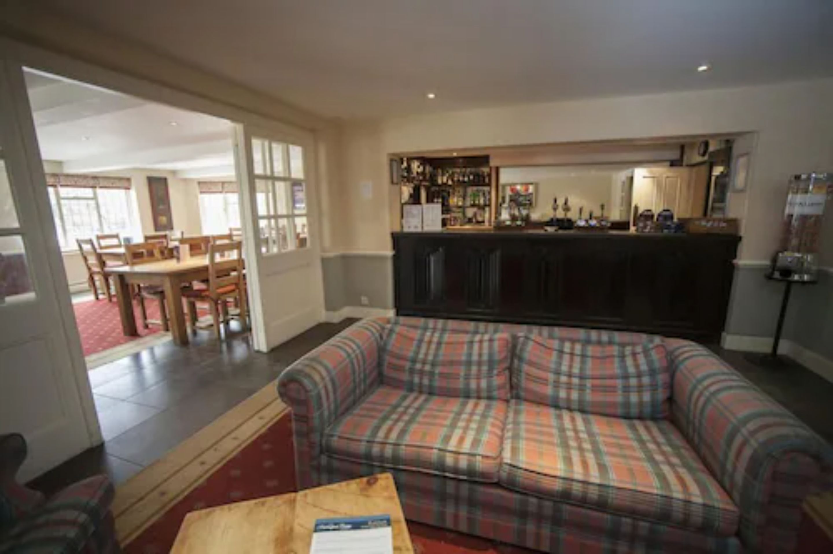 A living room with a plaid sofa, a wooden coffee table, and a bar area with various items.