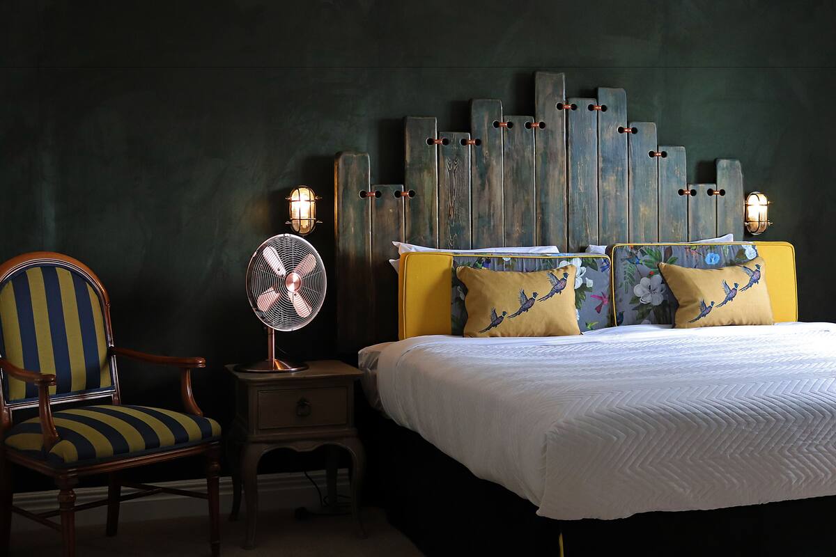 A bedroom with a bed, a chair, a bedside table, and a wall-mounted light fixture.