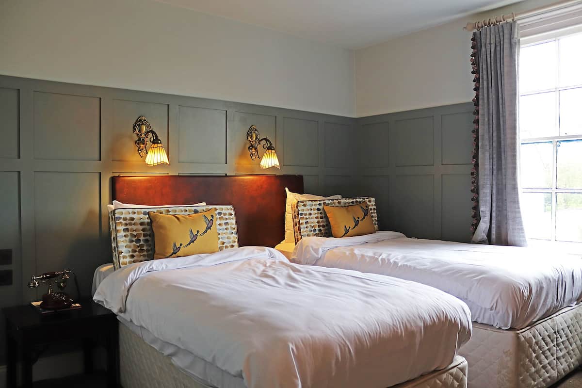A double bed with a headboard, two wall-mounted lamps, and a window with curtains.