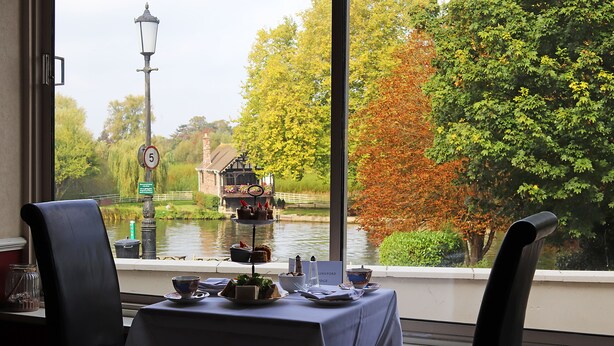 A dining table with a view of a river and trees. - Shillingford Bridge Hotel (Wallingford)