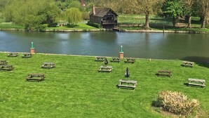 A riverside park with picnic tables and a traditional building by the water. - Shillingford Bridge Hotel (Wallingford)