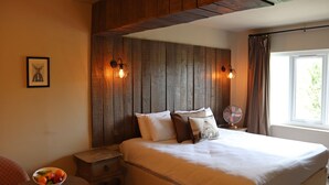 A bedroom with a wooden headboard, a bed with white bedding, a bedside table with a bowl of fruit, and a window with curtains. - Shillingford Bridge Hotel (Wallingford)