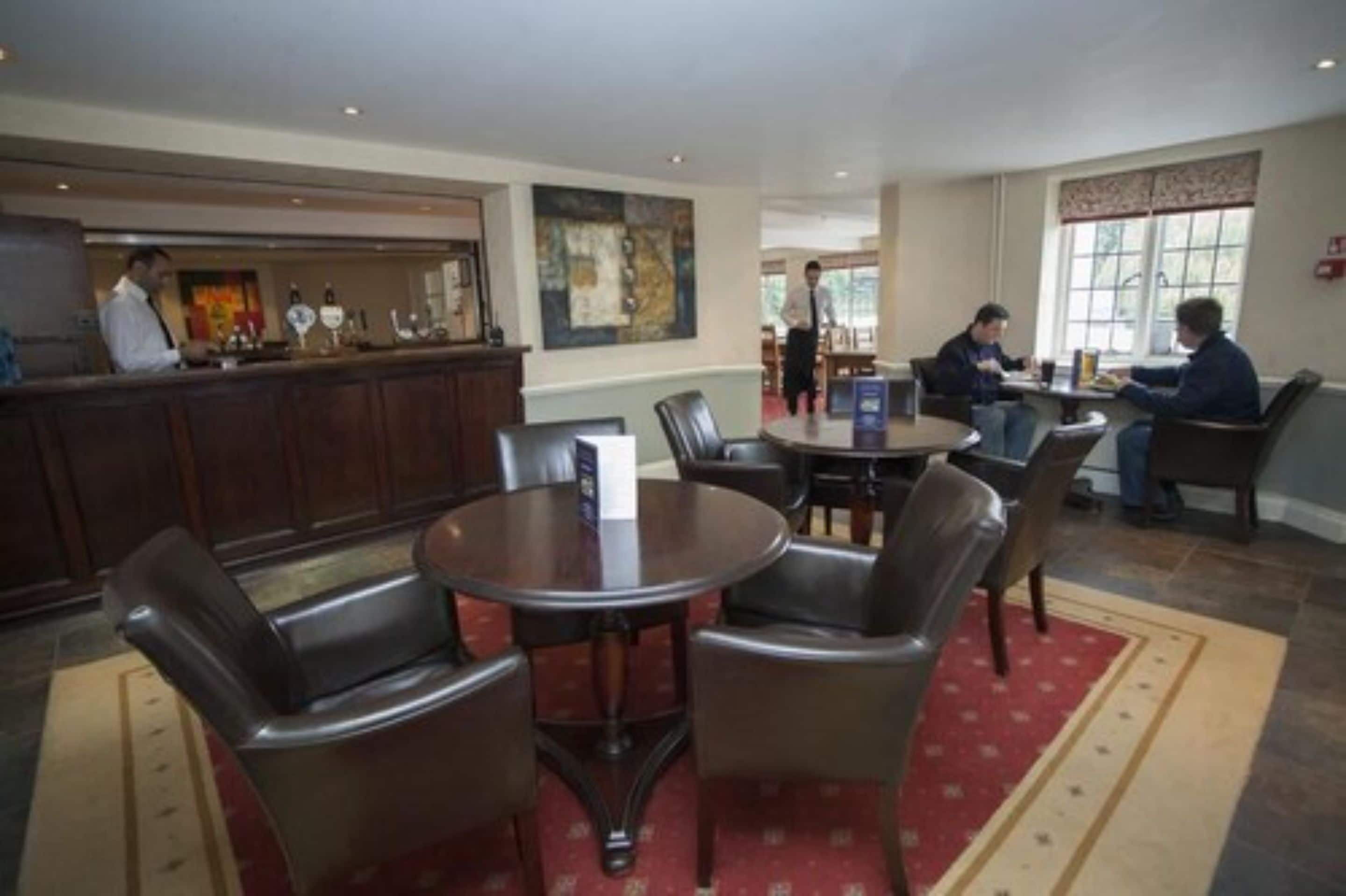 A hotel lobby with a reception desk, a dining area with round tables and chairs, and a large window with a view.