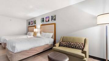 Habitación de hotel con dos camas, un sofá, una lámpara y obras de arte en la pared.