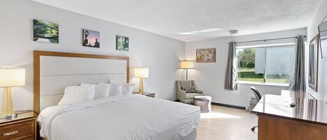 A hotel room with a large bed, bedside tables, a desk, a chair, and a window with a view.