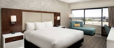 A hotel room with a large bed, a desk, a chair, and a view of the city.