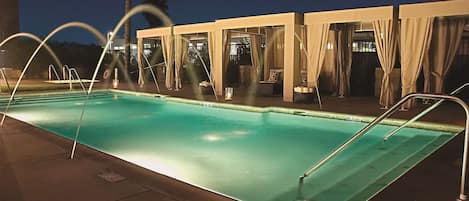 A swimming pool with a clear edge, surrounded by lounge chairs and covered seating areas.