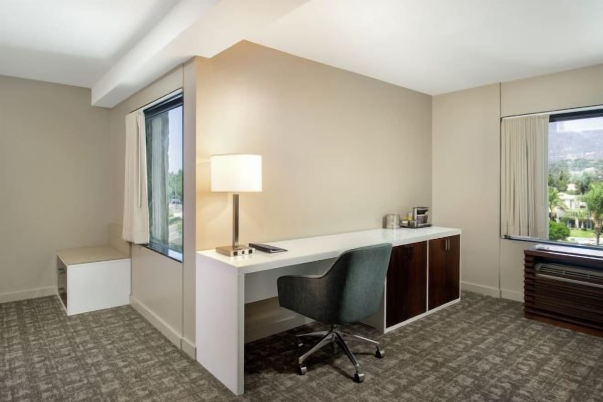 Une chambre d’hôtel équipée d’un bureau, d’une chaise, d’une lampe et offrant une vue sur le paysage urbain grâce à de grandes fenêtres.