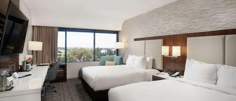 Habitación de hotel con dos camas, un escritorio, un televisor y ventana con vista a la ciudad.