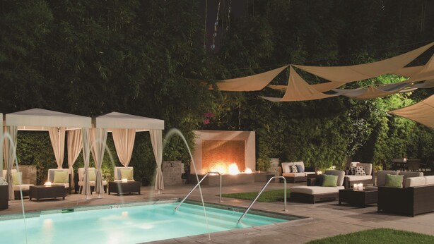 Un espacio de piscina exterior iluminado con sillones de descanso y una chimenea.