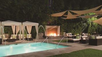 Relax by the pool surrounded by lush greenery and enjoy a comfortable seating area with lounge chairs and a sofa.