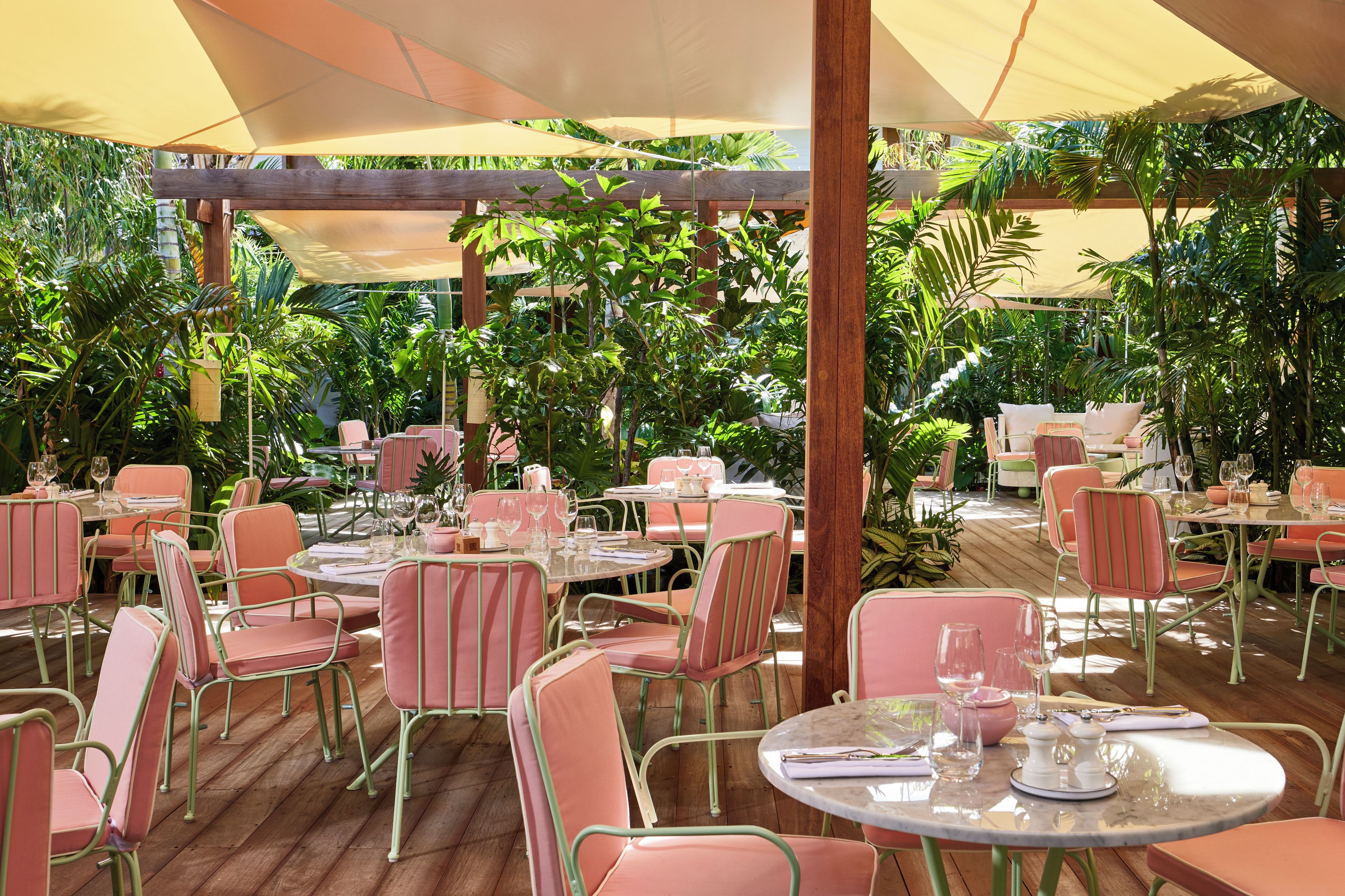 An outdoor dining area with round tables and chairs, surrounded by lush greenery.