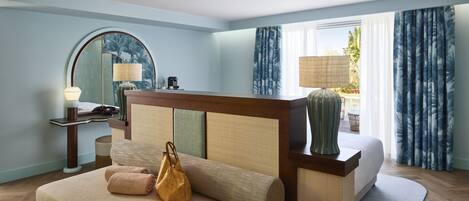 Habitación de hotel con cama, escritorio, lámpara, espejo y vistas al exterior.