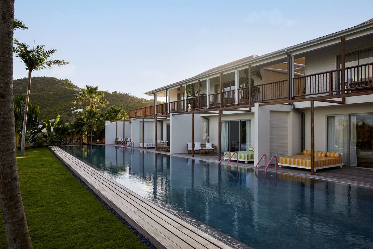 A modern hotel with a large pool, outdoor seating, and a view of a hill.