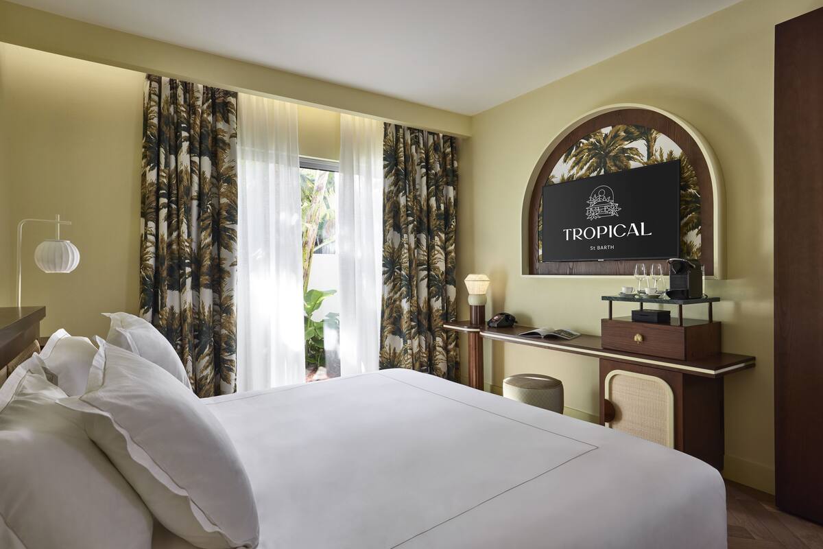 A hotel room with a bed, a desk with a lamp, a mirror, and a tropical-themed sign.