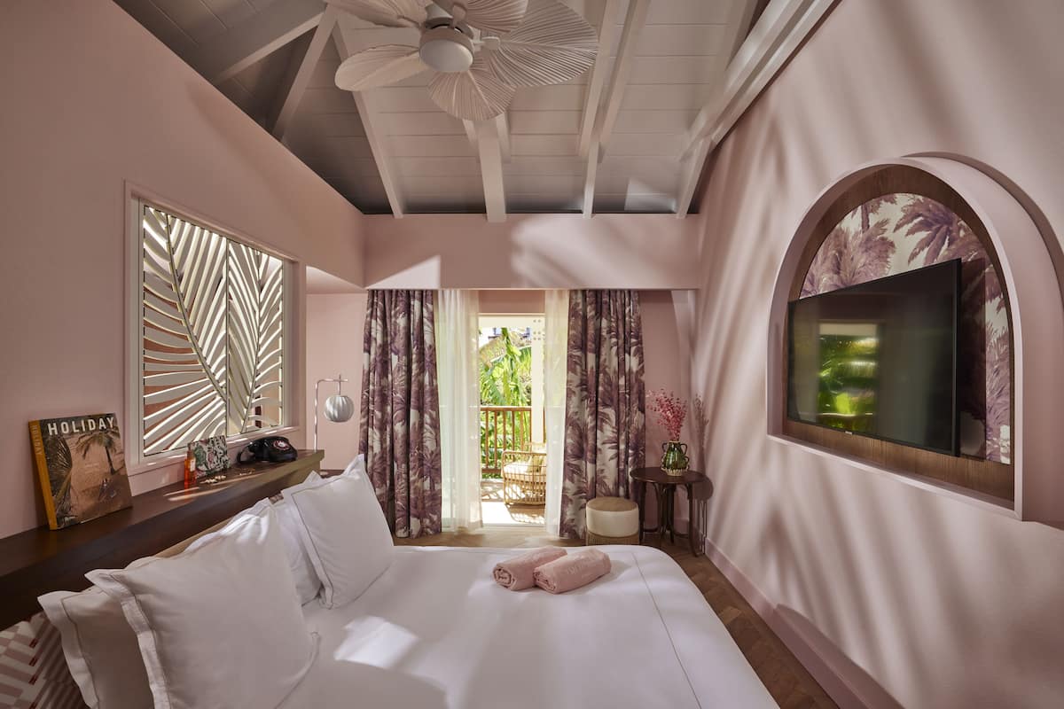 A hotel room with a bed, a ceiling fan, a TV, a window with curtains, and a view of the outside.