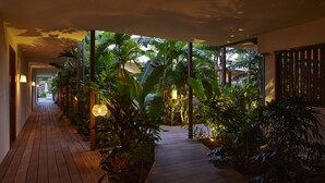 Un sendero de madera bordeado de exuberante vegetación tropical e iluminación ambiental, que conduce a la entrada de un edificio.
