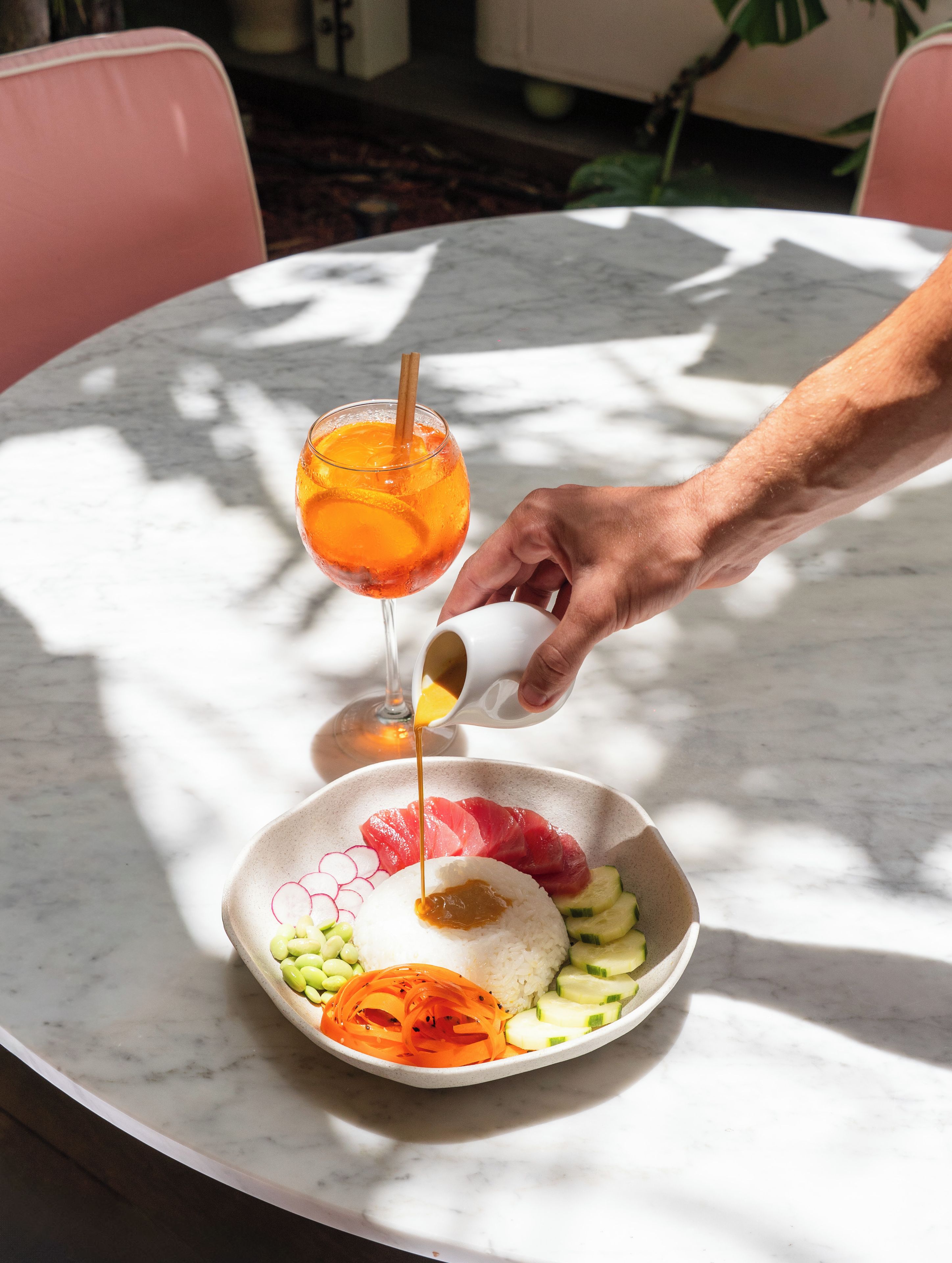 Une personne verse de la sauce sur un plat contenant du riz, du poisson et des légumes, le tout posé sur une table en marbre.