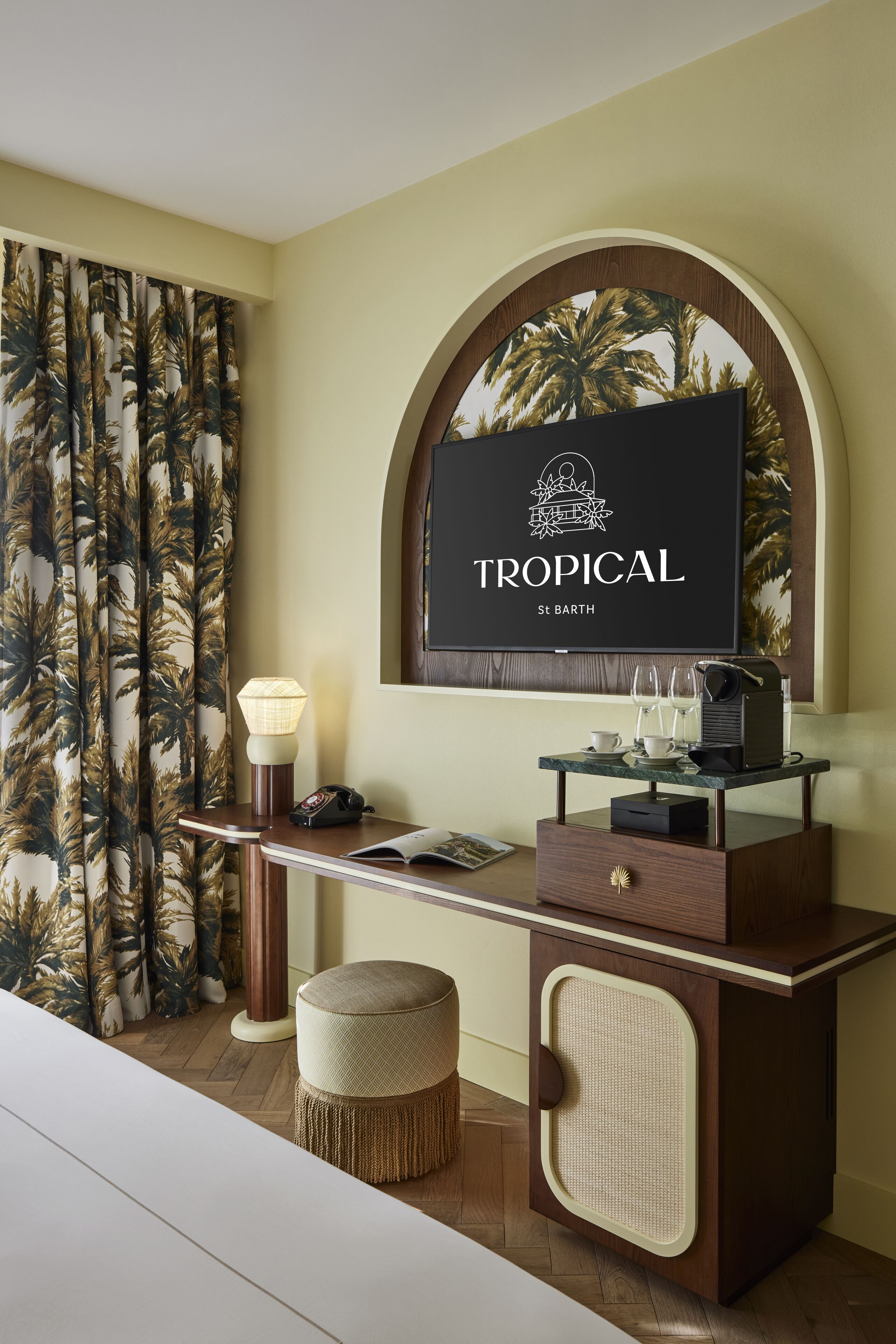 A room with a tropical theme, featuring a desk with a lamp, a telephone, and a small table with glasses and a book.