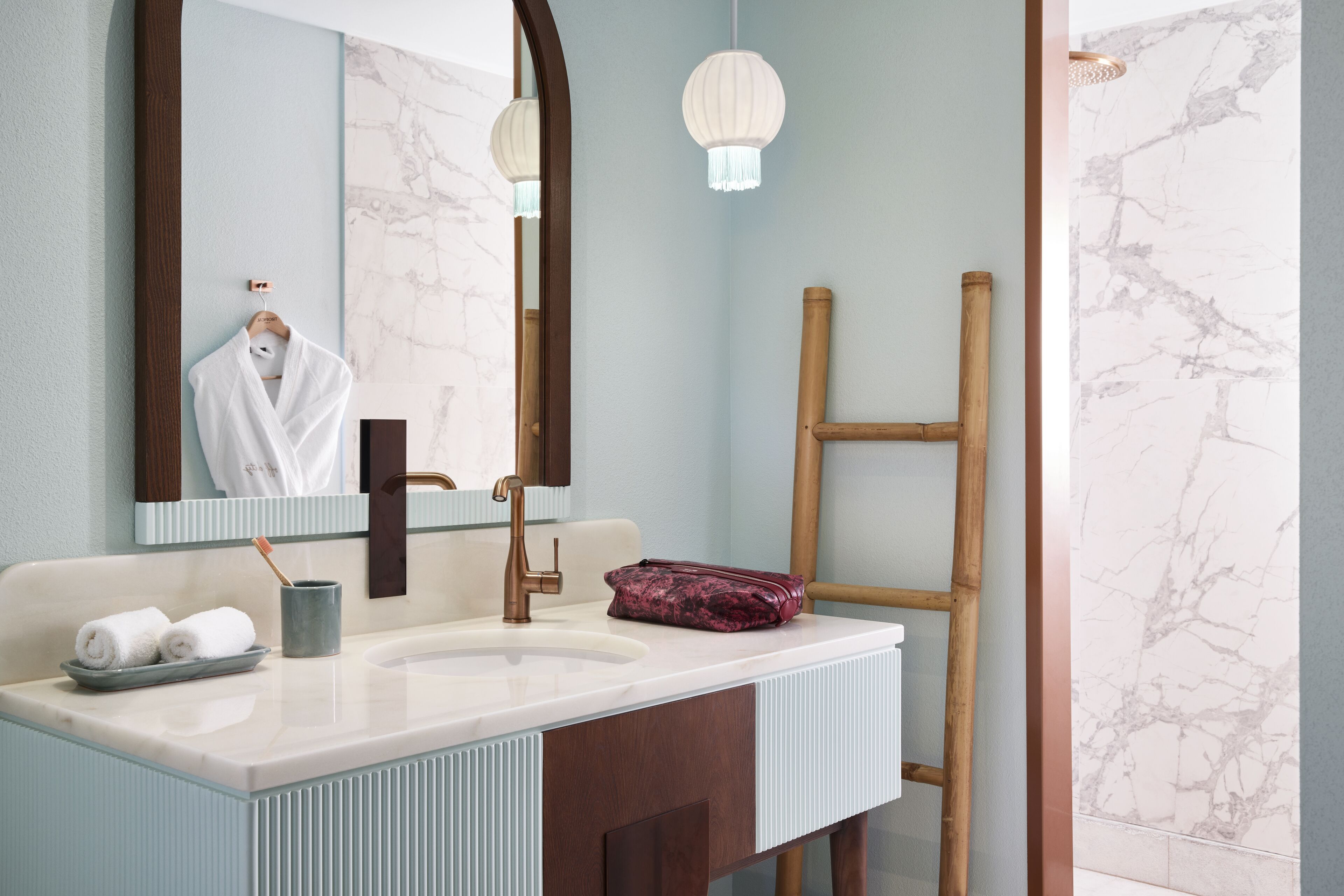 Une salle de bain avec un grand miroir, un lavabo muni d’un porte-serviettes, une échelle en bois et une lampe décorative suspendue.
