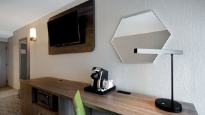 A modern hotel room with a wooden desk, a green chair, a flat-screen TV, a coffee machine, and a unique hexagonal mirror. - Holiday Inn Express Rochester - University Area by IHG (Rochester)