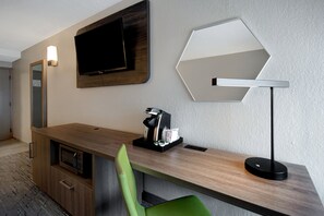 A modern hotel room with a wooden desk, a green chair, a flat-screen TV, a coffee machine, and a unique hexagonal mirror. - Holiday Inn Express Rochester - University Area by IHG (Rochester)