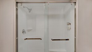 A glass-enclosed shower with a handheld showerhead, a towel rack, and a small shelf. - Holiday Inn Express Rochester - University Area by IHG (Rochester)