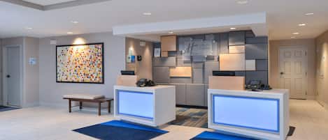 En hotellobby med modern design, som inkluderar en receptionsdisk, en sittgrupp och ett konstverk som hänger på väggen.