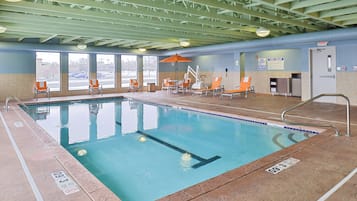 An indoor swimming pool with clear water, surrounded by lounge chairs and a covered seating area.