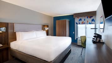 Una habitación de hotel con una cama grande, un armario, un escritorio con silla y una ventana con persianas.