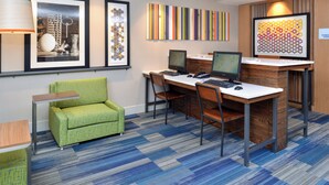 A hotel room with a desk, two monitors, a green armchair, and framed artwork on the wall. - Holiday Inn Express Rochester - University Area by IHG (Rochester)