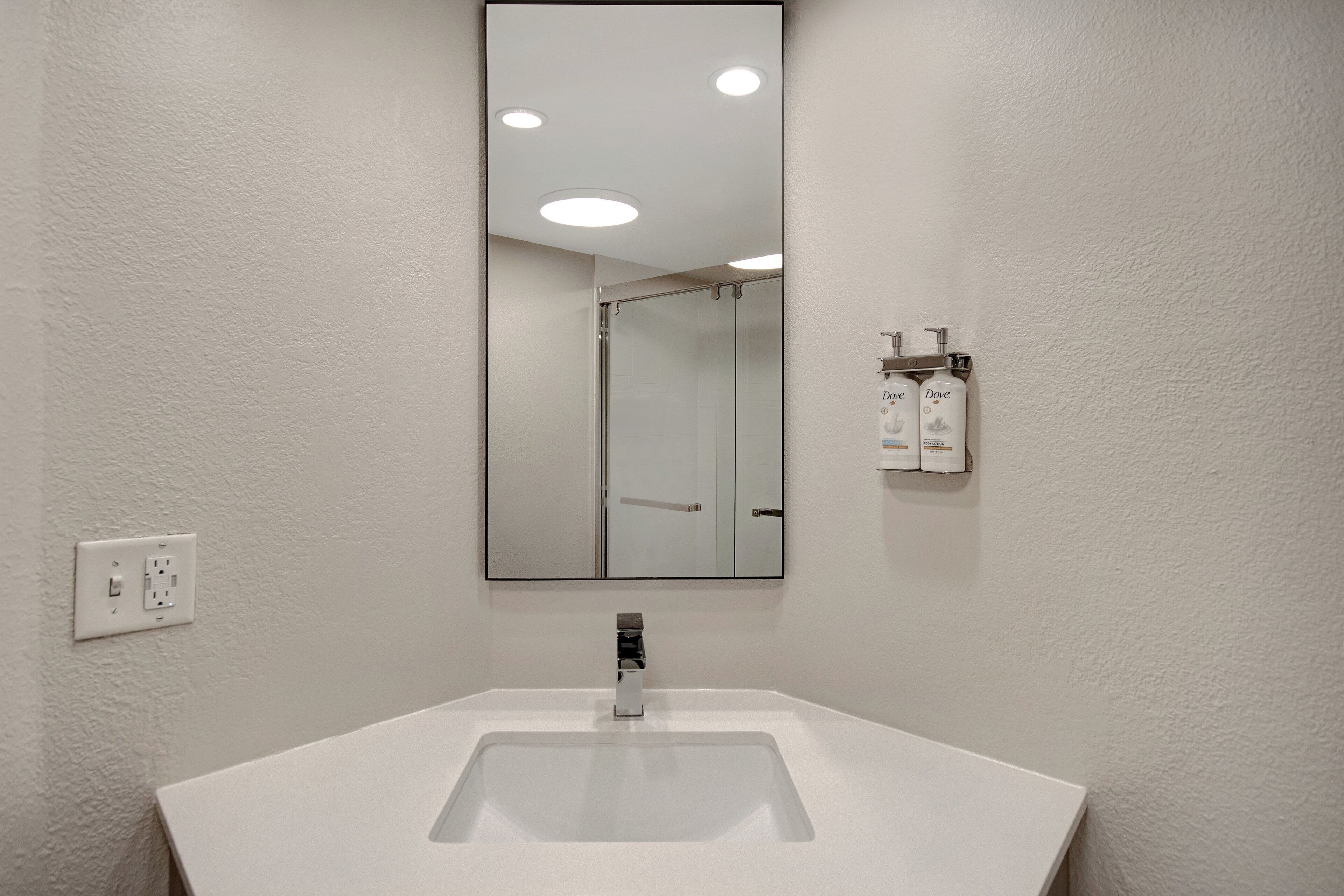 Un baño con lavamanos blanco, espejo y mampara de ducha.