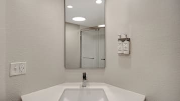 Un baño con lavamanos blanco, espejo y mampara de ducha.