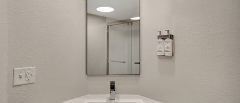 A bathroom with a white sink, a mirror, and a shower door.