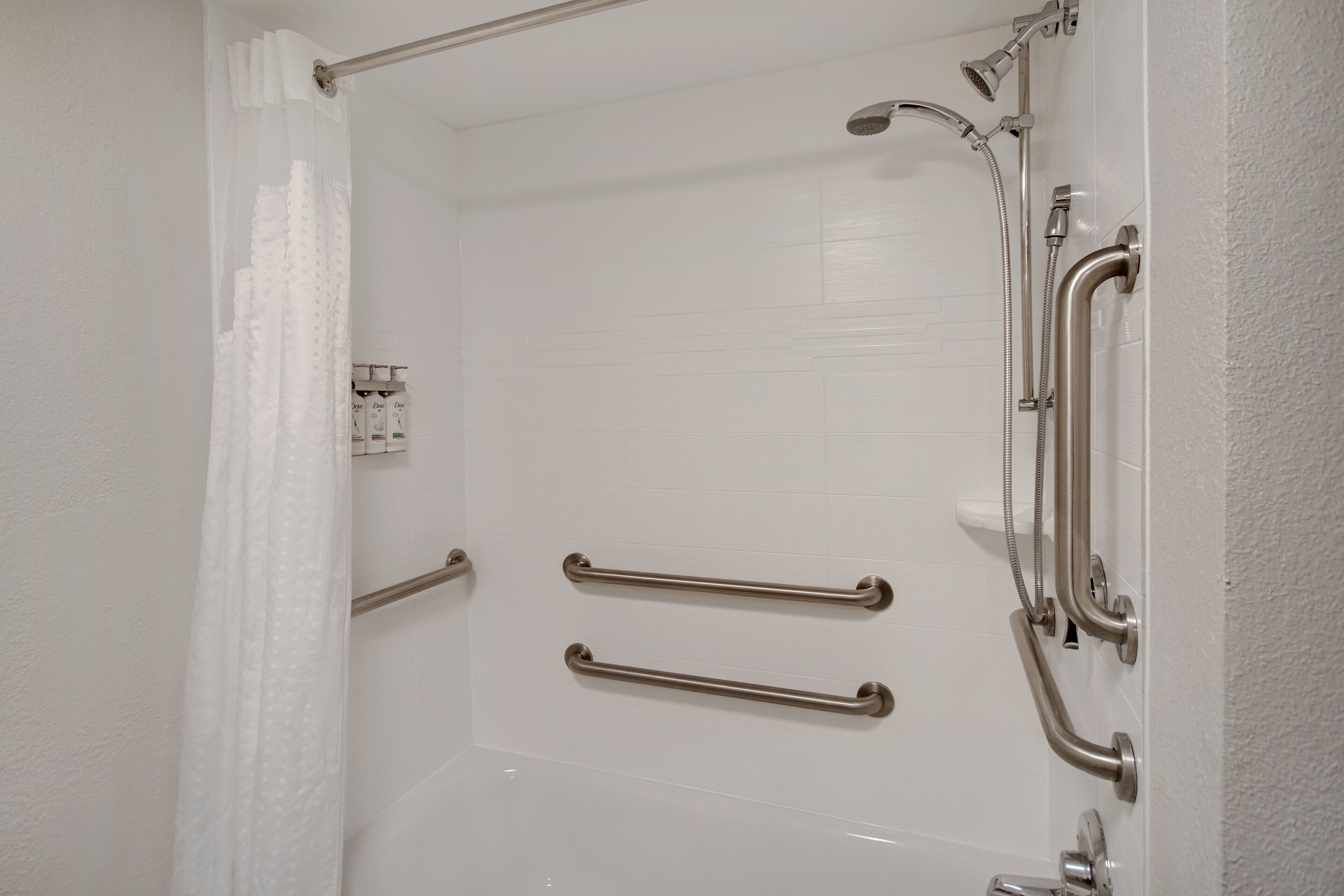 A white bathroom with a shower, grab bars, and a toilet.