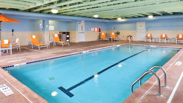 Una piscina interior con carriles claramente delimitados, una silla de salvavidas y una zona junto a la piscina con sillas y un escurreplatos.