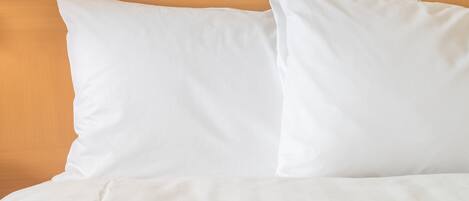 Een bed met witte beddengoed en kussens, tegen een houten hoofdbord.