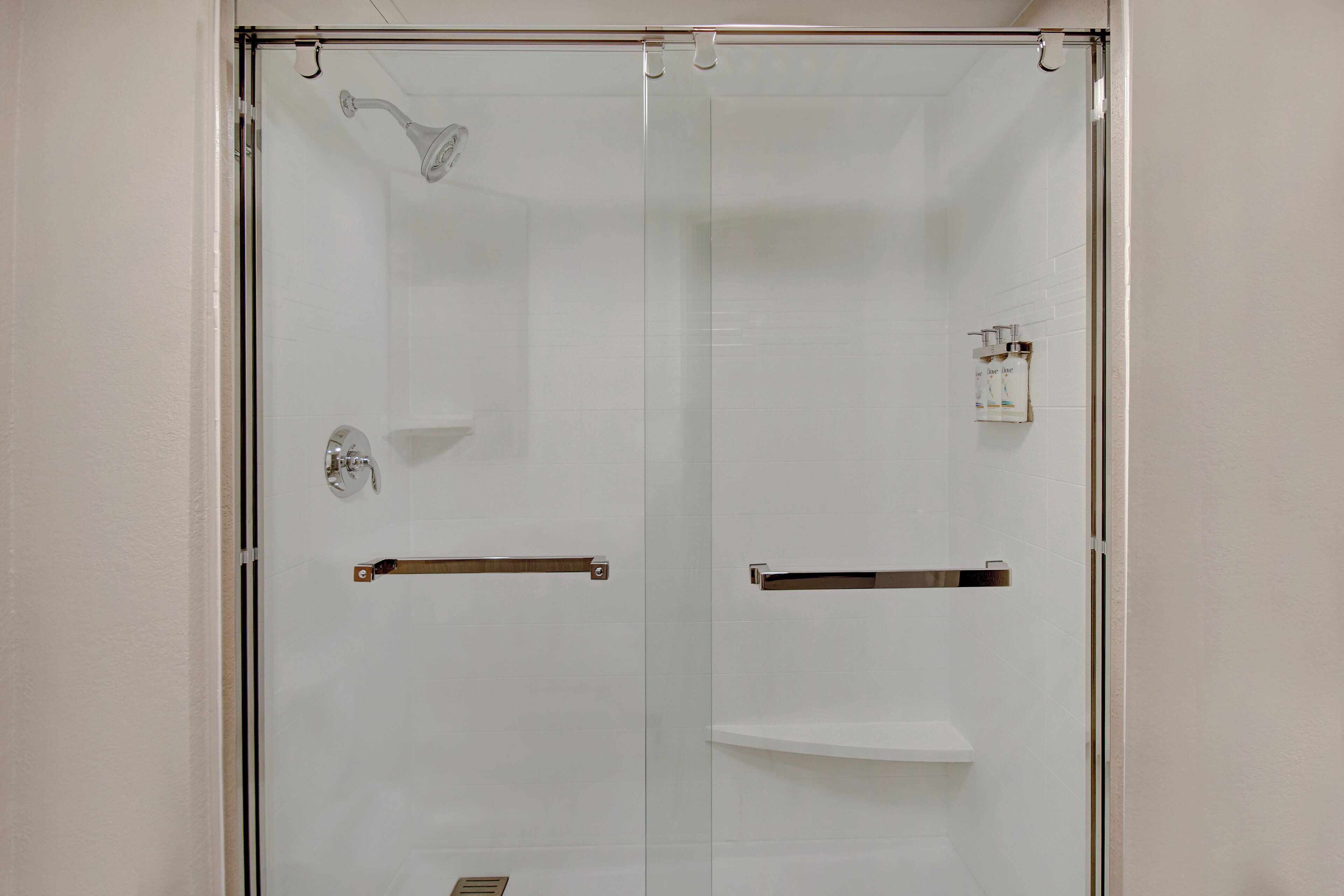A glass-enclosed shower with a handheld showerhead, a towel rack, and a soap dispenser.