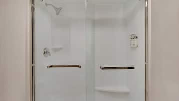 A glass-enclosed shower with a handheld showerhead, a towel rack, and a soap dispenser.