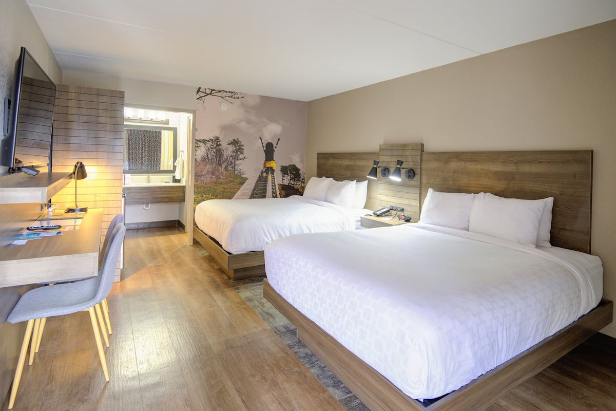 Una habitación de hotel con un escritorio de madera, dos camas, un espejo grande y un mural en la pared.