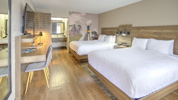 Habitación de hotel con dos camas, un escritorio con silla, un espejo y un mural en la pared.