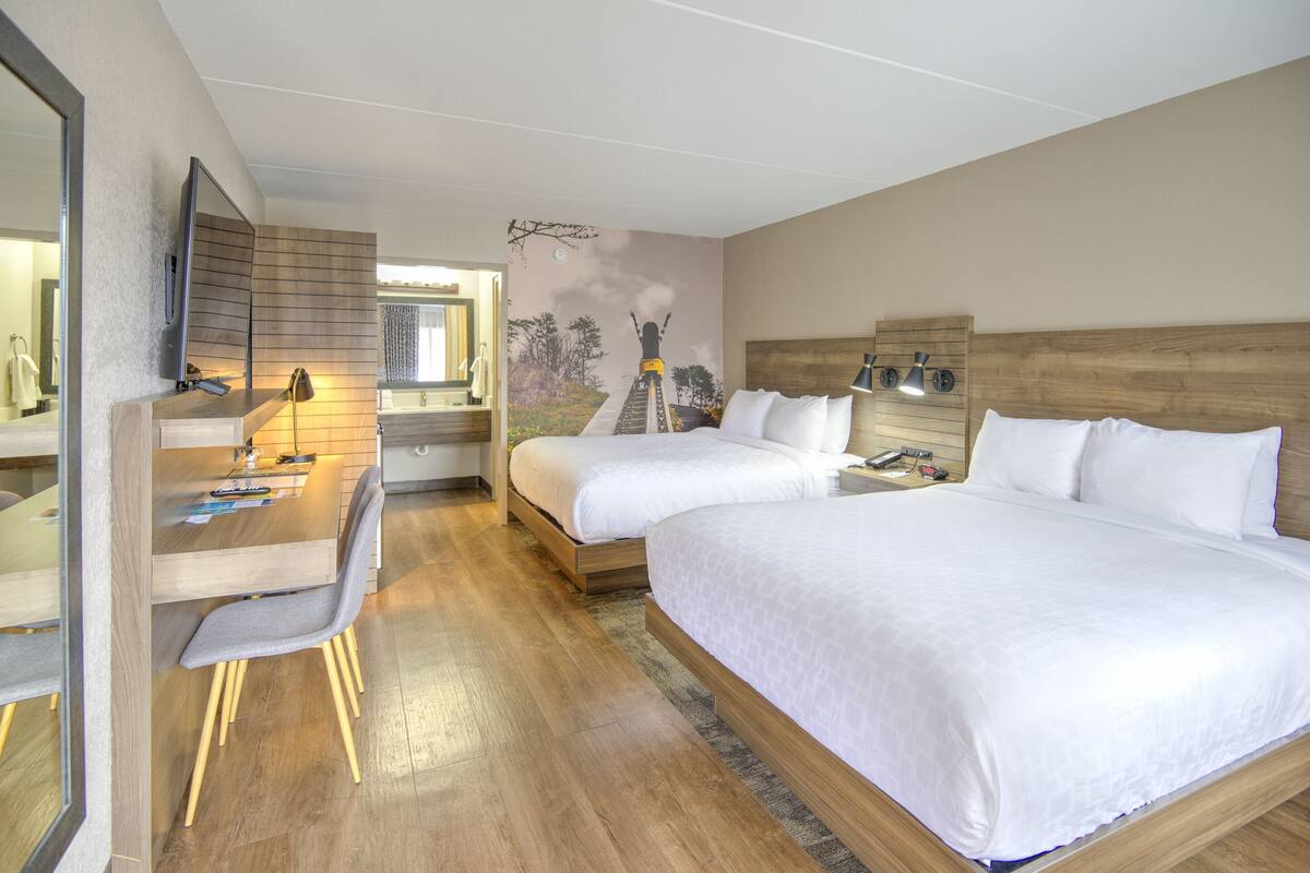 Habitación de hotel con dos camas, un escritorio con silla, un espejo y un mural en la pared.
