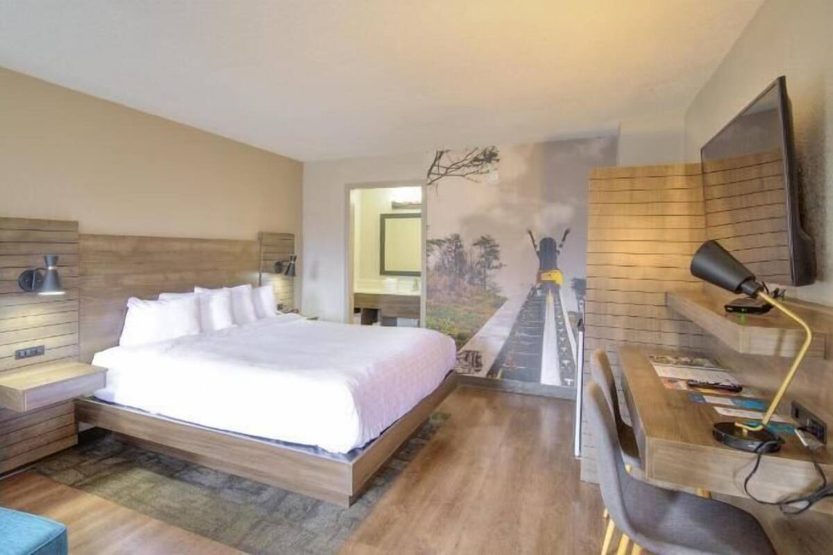 Un dormitorio con cama, escritorio, silla y televisión instalada en la pared.