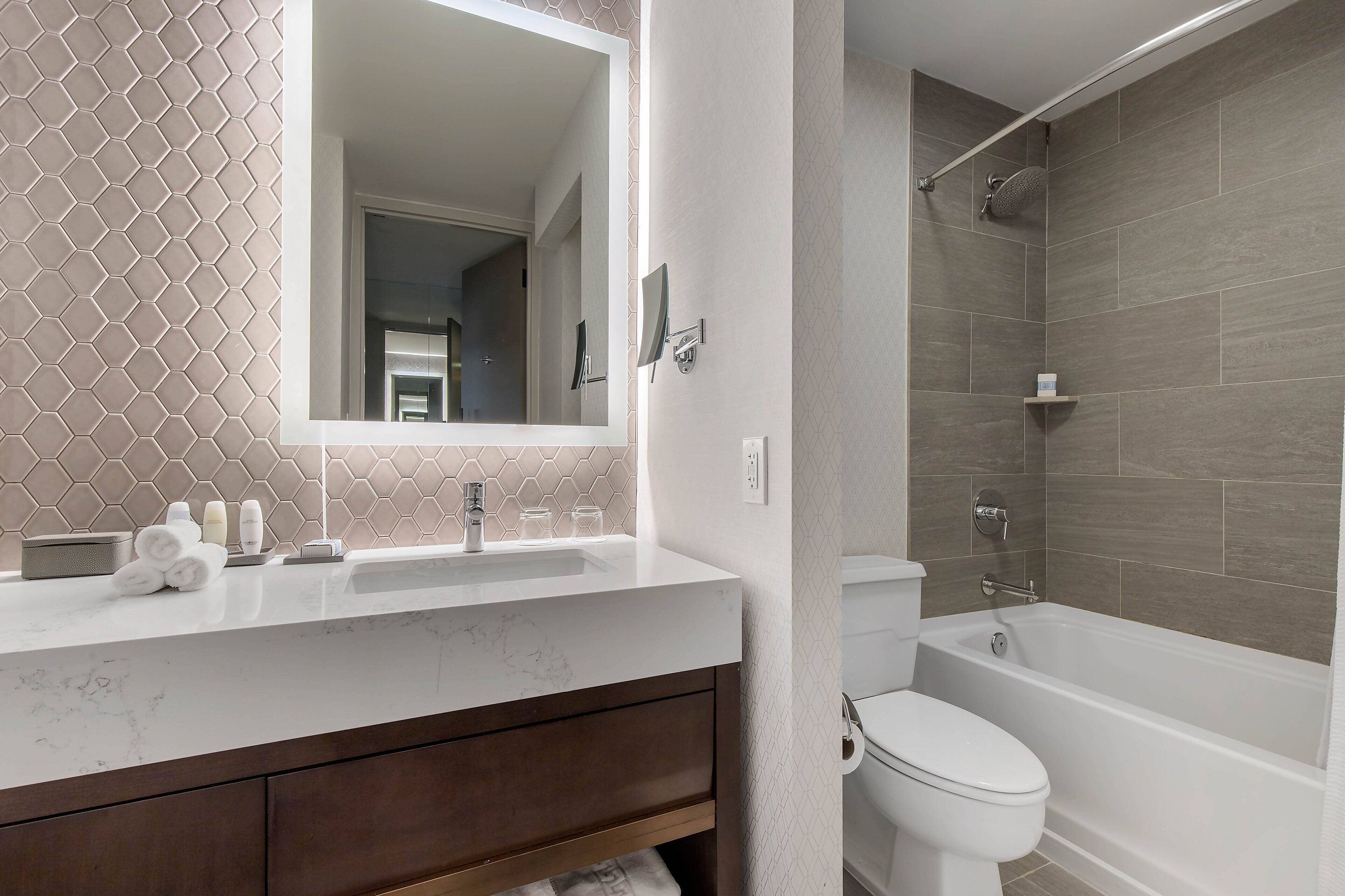 A modern bathroom with a marble sink, a large mirror, a toilet, and a shower area.